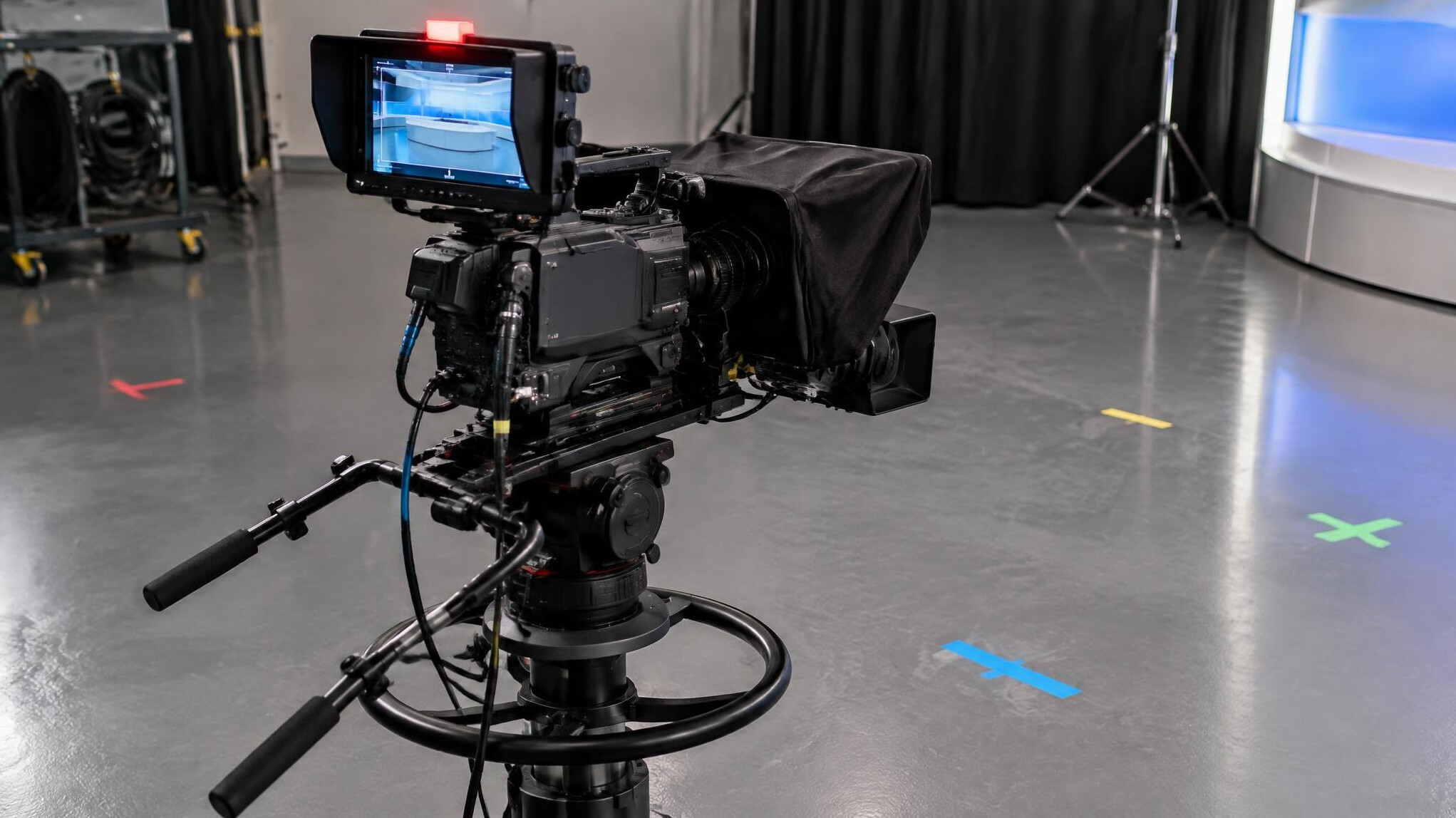 Shoulder-mounted broadcast camera rig on a studio floor with rehearsal marks